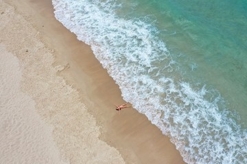 girl in a red bathing suit lies on the shore of a sandy beach with turquoise water yalong bay