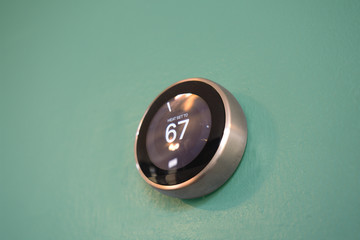 Smart home thermostat on green background. Heating house efficiently to 67 degrees. Light mint wall...