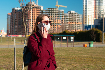 girl in sunglasses on the street talking on a cell phone. on the face is a white protective mask....