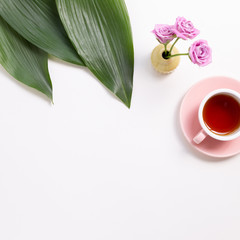 Cup of black tea with green leaves and flowers on white background. Flat lay, top view, copy space