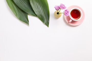 Obraz premium Cup of black tea with green leaves and flowers on white background. Flat lay, top view, copy space