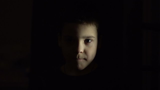 A boy is standing in the dark. Not expressive face. Without emotion. Close-up. Education.