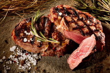 Grilled beef steak with rosemary, salt and pepper on black stone plate. Grilled striploin sliced...