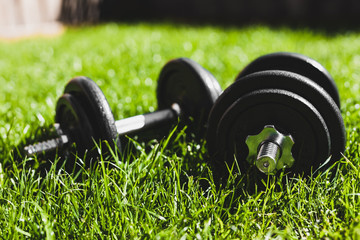 keeping fit and exercising outdoor, set of heavy dumbbells on green grass lawn in a backyard under direct sunlight