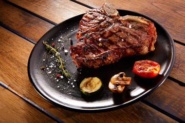 Grilled beef steak with rosemary, salt and pepper on black stone plate. Grilled striploin sliced steak. Juicy thick grilled beef steak seasoned with rosemary fresh of the summer BBQ.