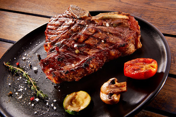 Grilled beef steak with rosemary, salt and pepper on black stone plate. Grilled striploin sliced steak. Juicy thick grilled beef steak seasoned with rosemary fresh of the summer BBQ.