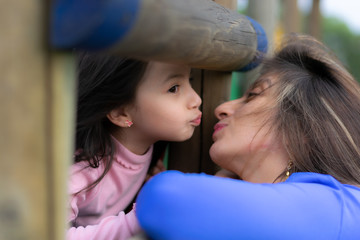 beautiful Colombian Latin American mother and daughter playing in a city park in Bogotá kiss each...