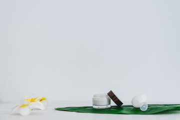 vegan natural beauty, pot of face cream and bottle of body lotion on tropical green leaf with monoi flowers
