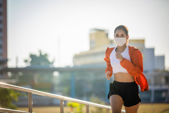 Asian Young fitness sport woman running  and she wears a mask for protective Dust and pollution and protection flu virus, influenza, coronavirus on city