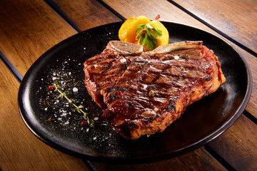Grilled beef steak with rosemary. Grilled striploin sliced steak. Juicy thick grilled T-bone beef steak seasoned with rosemary fresh of the summer BBQ. Vegetables on a black plate with salt and pepper