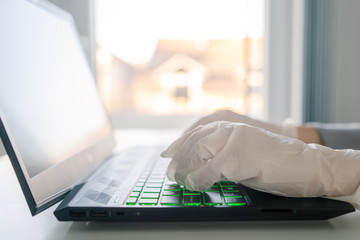 Close up on hands of female woman wearing white protective gloves while working on laptop