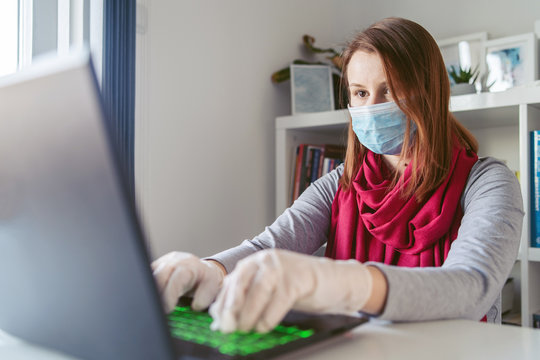 Young woman caucasian wearing gloves on hands and mask on face while working from home or at the office work by the table laptop in day preventing virus spread during epidemic quarantine prevention