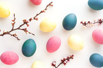 Stylish easter background with colored natural dyed eggs and flowering branches on white desk. Zero waste Easter concept. Flat lay, top view.