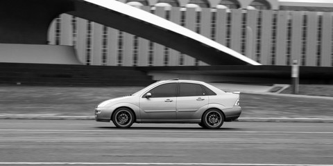 Obraz premium Ford Focus em panning na frente de construção de concreto em preto e branco
