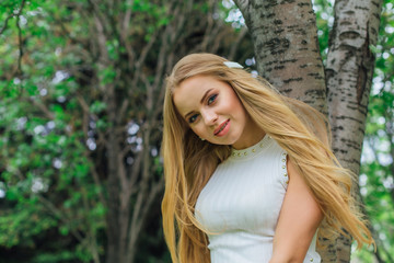 Portrait of a charming blond woman wearing beautiful white dress standing next to rowan tree.