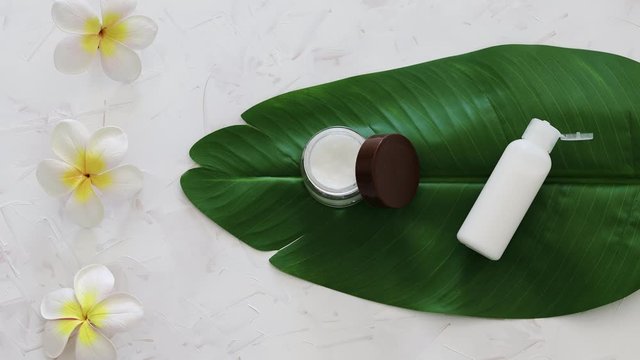 natural beauty without harsh chemicals, pot of face cream and bottle of body lotion on tropical green leaf with monoi flowers and camera defocusing