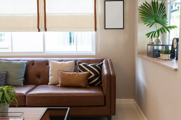 Brown leather sofa with graphic pattern pillow in elegant living room interior by the window. Modern stylish interior.