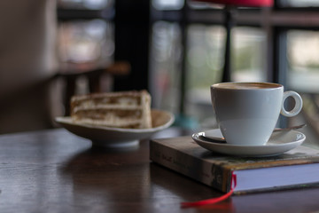 white cup of coffee capuccino over a book in a coffee shop tiramisu out of focus