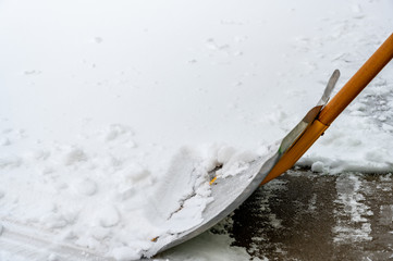 aluminum shovel being used to scoop snow from concrete driveway 