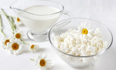 Homemade cottage cheese and cream in glassware. on a white background. Soft focus. Chamomile flowers as a symbol of rustic.  Copy Space
