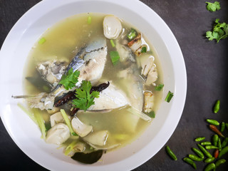 Top view of Spicy Mackerel Soup (Tom Yum Pla Tu)Thai traditional local food in white bowl on dark background, spicy hot & sour soup with herbs.