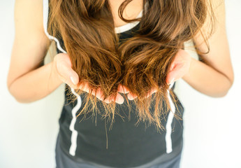 Cropped shot view of woman holding her damaged split ended hair (Focus at ends hair). Hair damage is risk for further damage and breakage. It may also look dull or frizzy and be difficult to manage.
