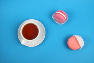 Obraz na płótnie Canvas cup of tea and two macaroons on blue background flat lay