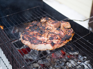 A large piece of meat is cooked on a charcoal grill. Cooking outdoors
