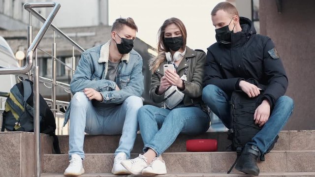 Young people are sitting on stairs outside a bulding wearing black masks.