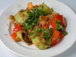 Hot salad of zucchini and pepper on a round white plate. Close-up