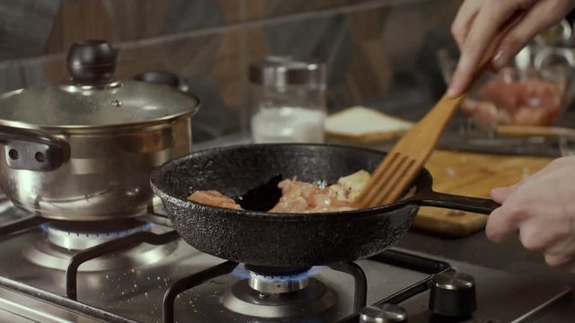Mixing chicken meat in frying pan with wooden shovel, shallow depth of field, slow motion