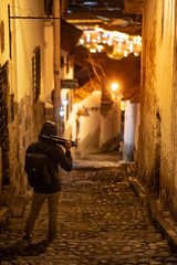 Fototapeta na wymiar Hoody photographer man holding tripod standing in alley in Cusco (Cuzco), Peru. Historical inca empire city exploration at night. Mystery city concept