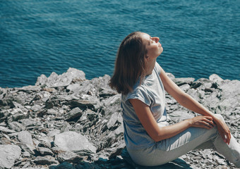 the girl is sitting on the rocks by the lake. Woman sunbathing on the beach. The concept of recreation, tourism