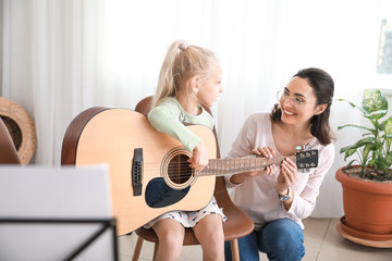 Private music teacher giving guitar lessons to little girl at home