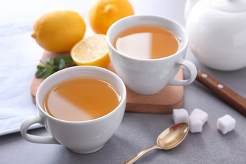 Cups of hot tea with lemon on grey background