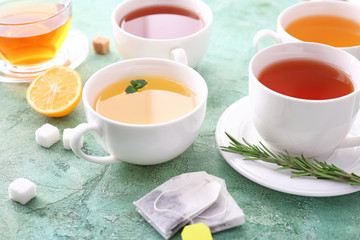 Cups with different types of hot tea on color background