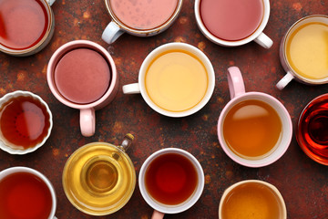 Cups with different types of hot tea on color background