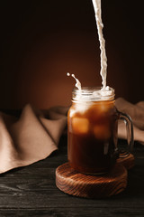 Pouring of milk into cold coffee in mason jar on table