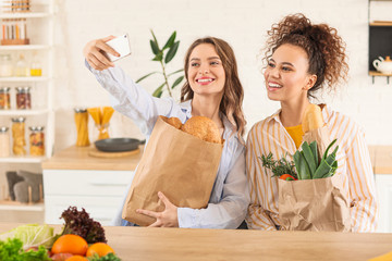 Young women with fresh products from market taking selfie at home