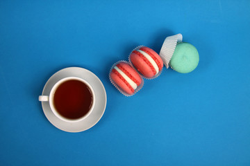 cup of tea and macaroons of different colours on blue background flat lay