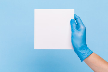 female hand in a  medical glove holds a blank form of paper on a blue background. Mock up, business card