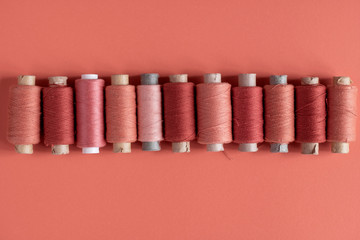 A pink spool of threads on coral paper background, with copy space.