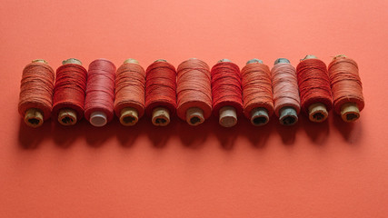 A coral spool of threads on coral paper background, with copy space.