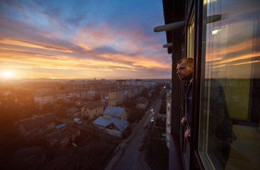 Side view of a smiling man looking away from a balcony at sunset. Beautiful city landscape of a...