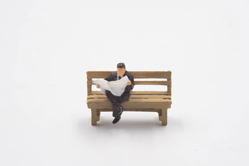 The miniature businessman sitting reading newspaper in the bench isolate on white background
