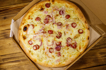 Delicious fresh pizza in cardboard box on a wooden table. Top view. Concept for home delivery of food, fast food, delivery of pizza