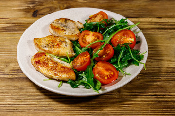 Fried chicken breast with salad of fresh arugula and cherry tomatoes on wooden table