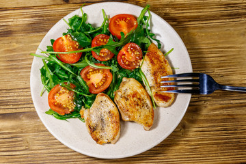 Fried chicken breast with salad of fresh arugula and cherry tomatoes on wooden table. Top view