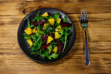 Tasty salad of fresh arugula, beetroot and oranges on wooden table. Top view. Healthy food or vegetarian concept