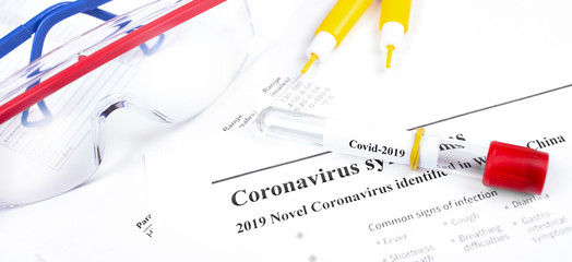 Glass tube with text Coronavirus (Covid-2019), lancets and antibacterial safety glasses on the work papers closeup background